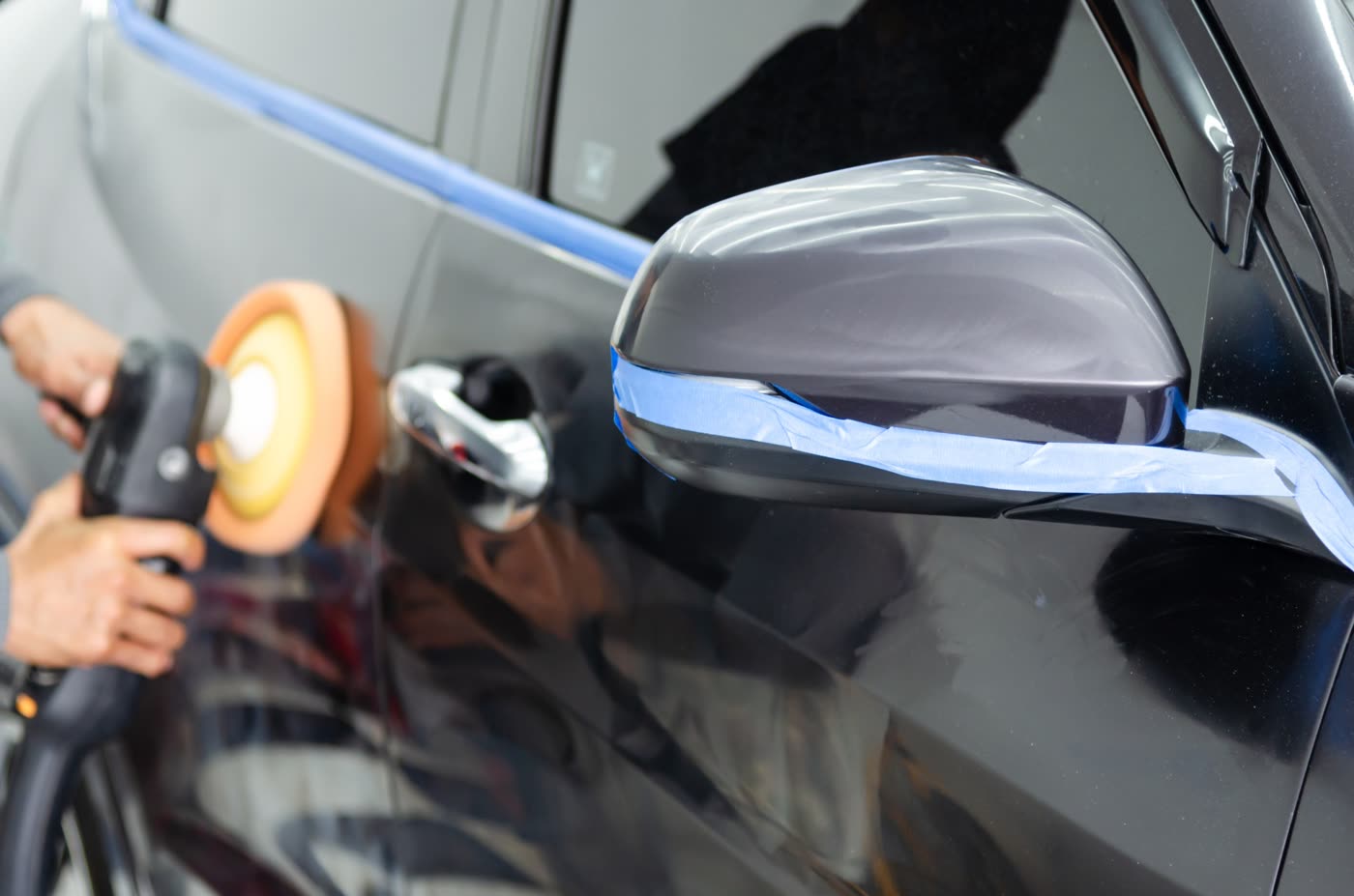 Masking tape being applied around a wing mirror before machine polishing